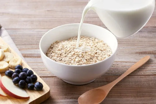 bol de overnight oats dans lequel on verse du lait, posé sur une table de cuisine à côté de fruits